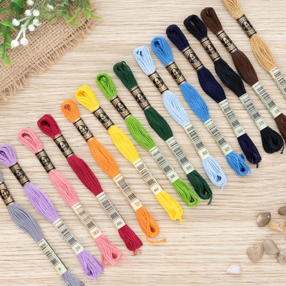 Set of colorful DMC sashiko embroidery threads on a wooden surface with pebbles and greenery.