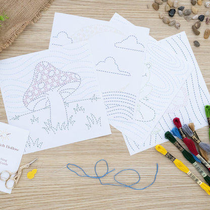 Sashiko-inspired Embroidery Sheets displayed on a wooden board. Mushroom in field, Moon over waves, Frog on Pond and Flower in night sky.