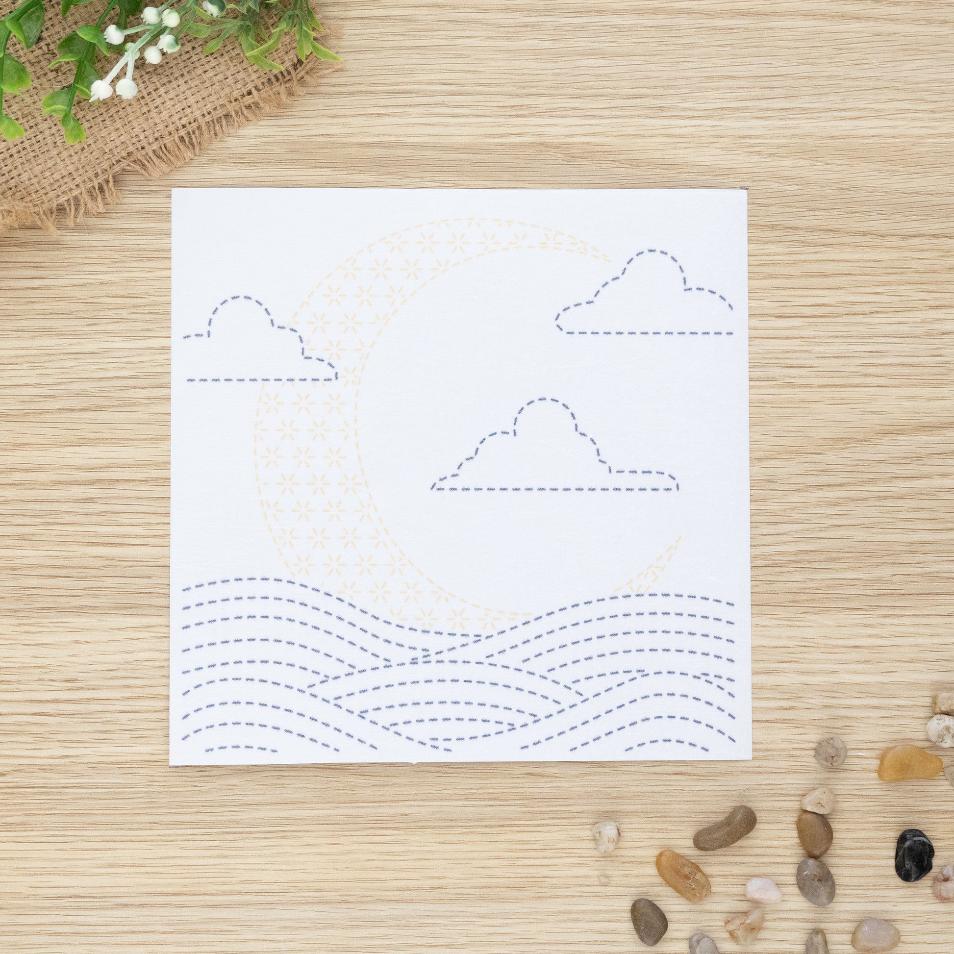 Sashiko embroidery transfer sheet of moon over waves, displayed on wooden background
